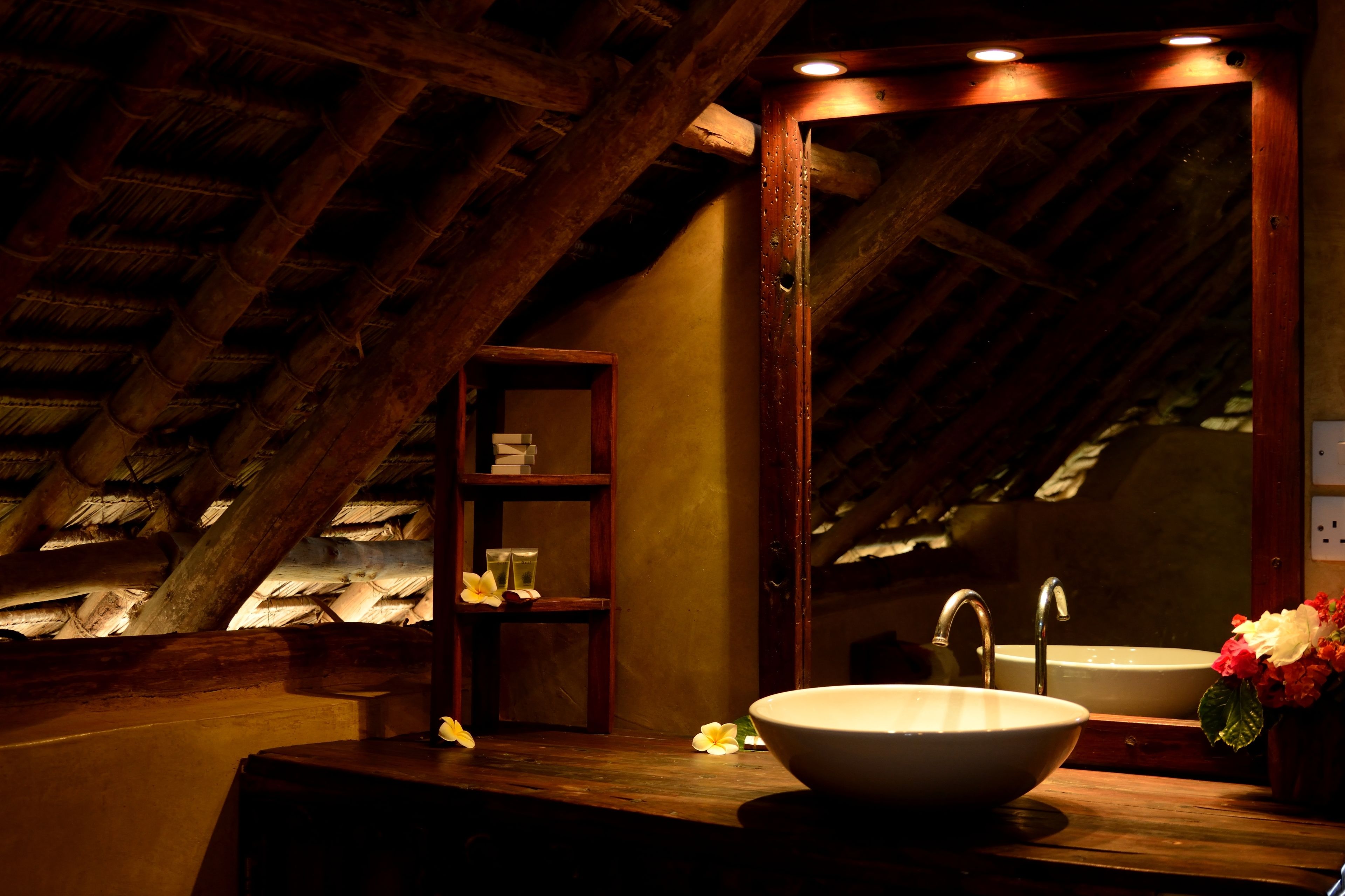 A bathroom with a wooden vanity, two sinks, a mirror, and a shelf with toiletries.