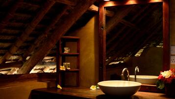 A bathroom with a wooden vanity, two sinks, a mirror, and a shelf with toiletries.