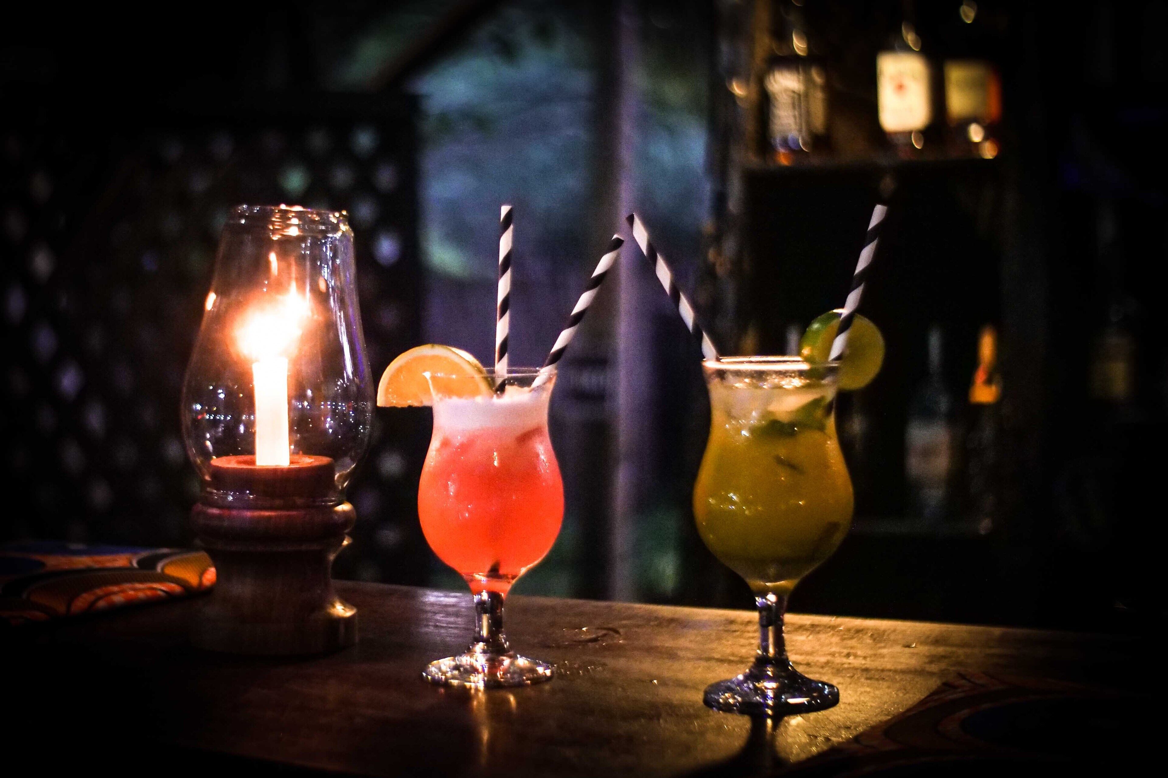 Three cocktails on a bar counter with a candle in a glass jar.