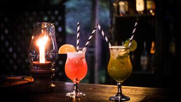 Three cocktails on a bar counter with a candle in a glass jar.