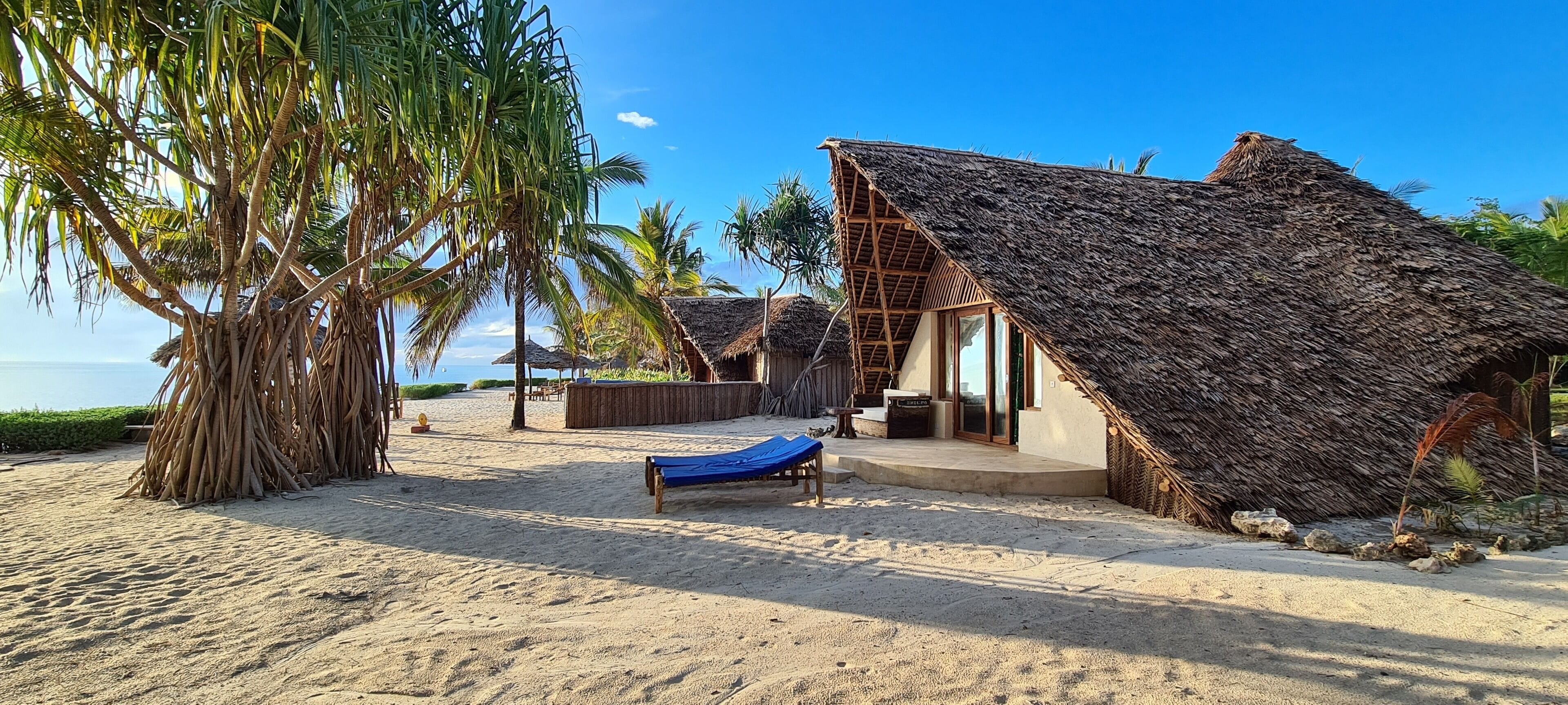 A beachside resort with thatched-roof huts, a sandy beach, and a palm tree.