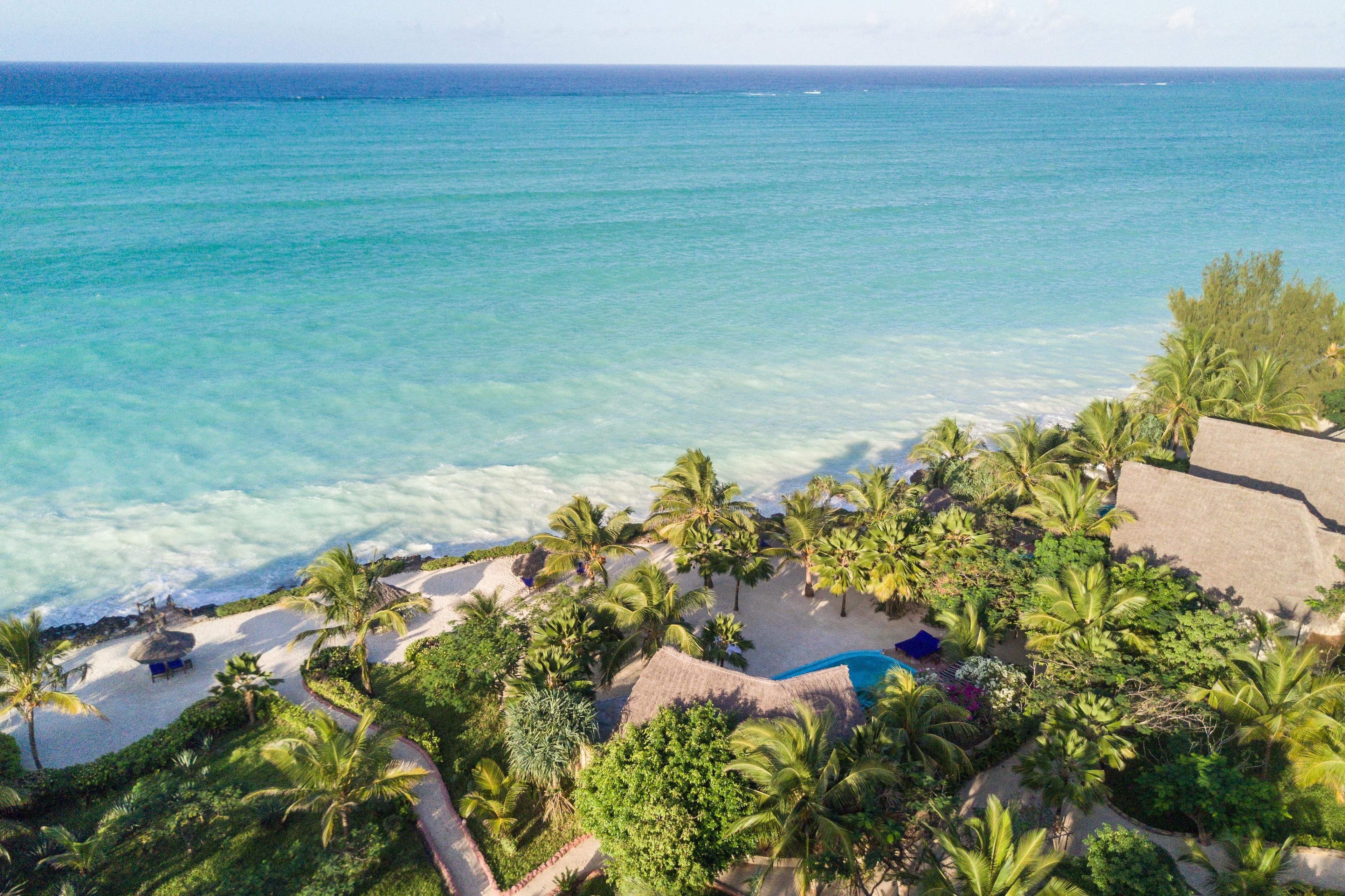 Un resort de playa tropical con vista clara al océano, palmeras y una piscina.