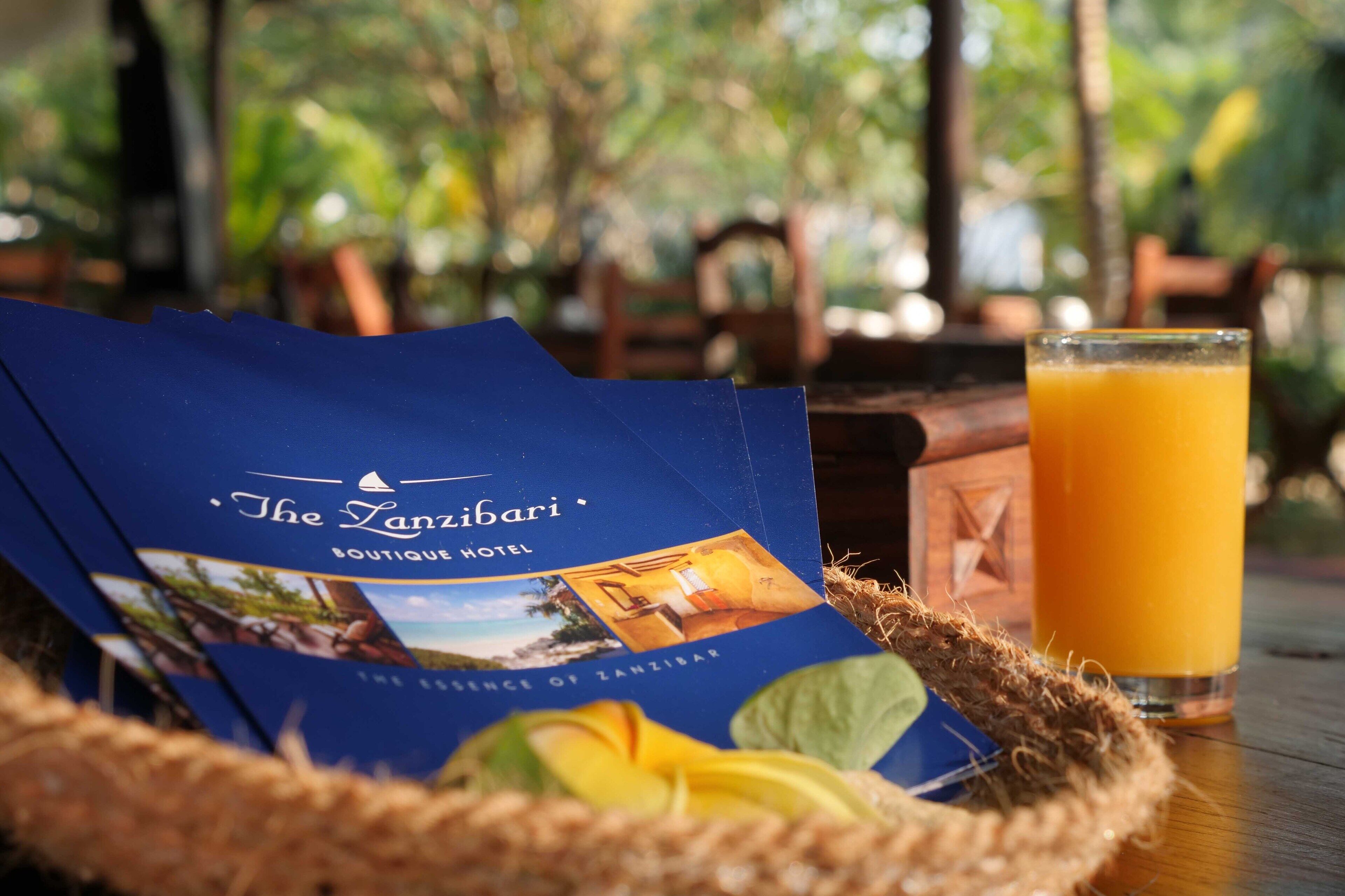 Une brochure de l’hôtel-boutique Tanzibari, avec un verre de jus d’orange posé sur une table en bois.