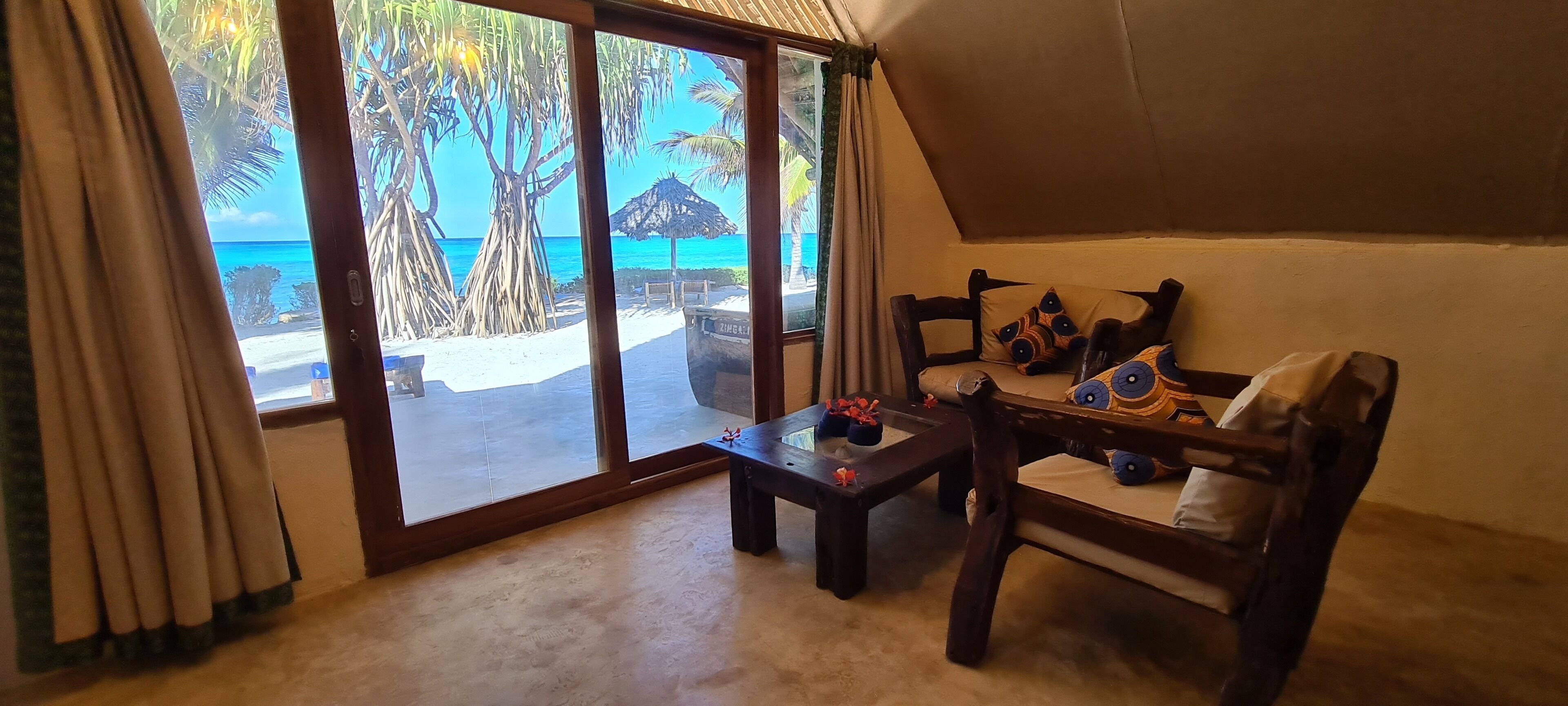 Une chambre avec vue sur la plage, une chaise en bois, une petite table et une fenêtre avec des rideaux.