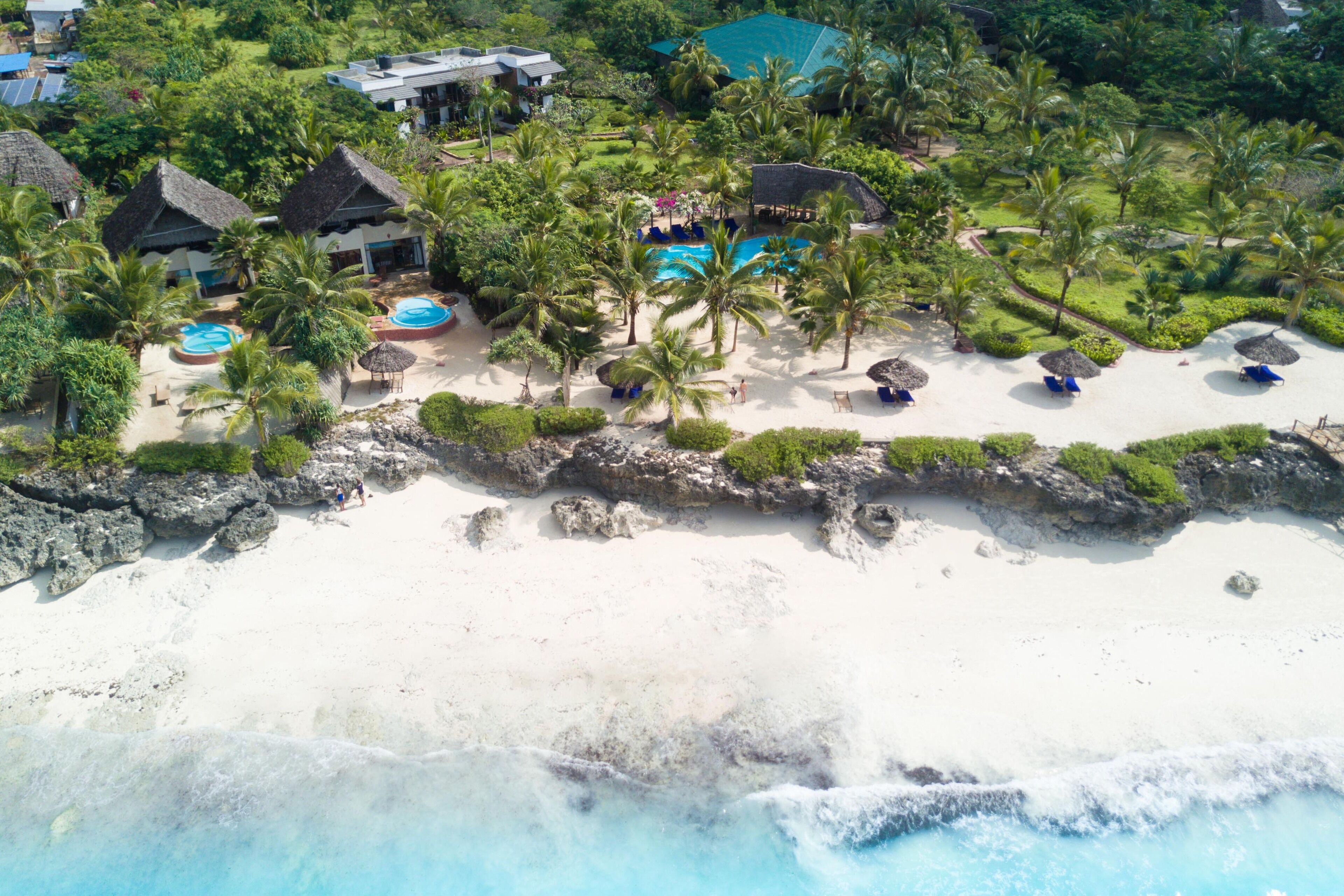 Oversigtsbillede af et resort med strand, palmer og poolområde.