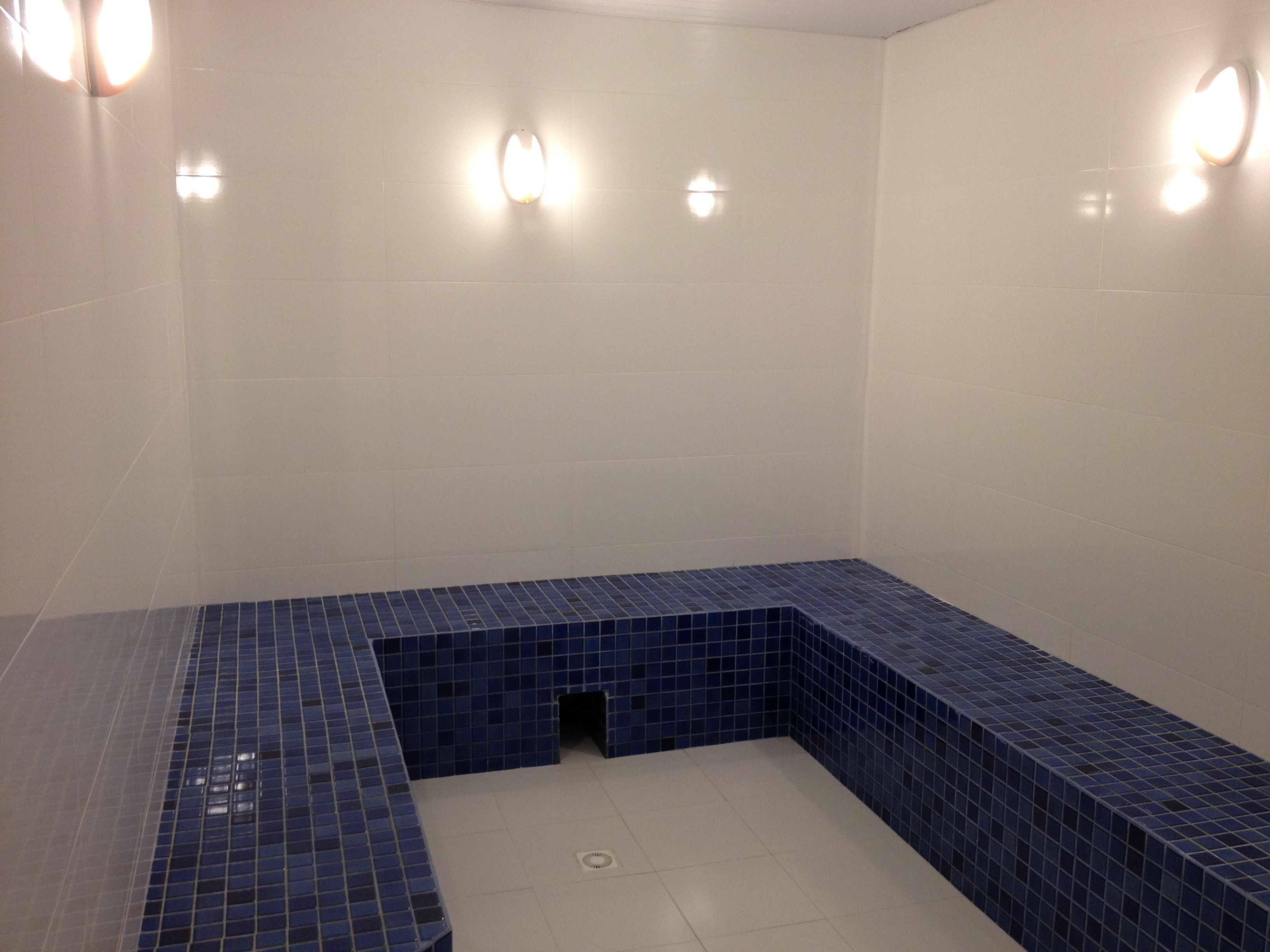 Une salle de bain aux murs blancs, avec un banc recouvert de carreaux bleus et trois appliques murales.