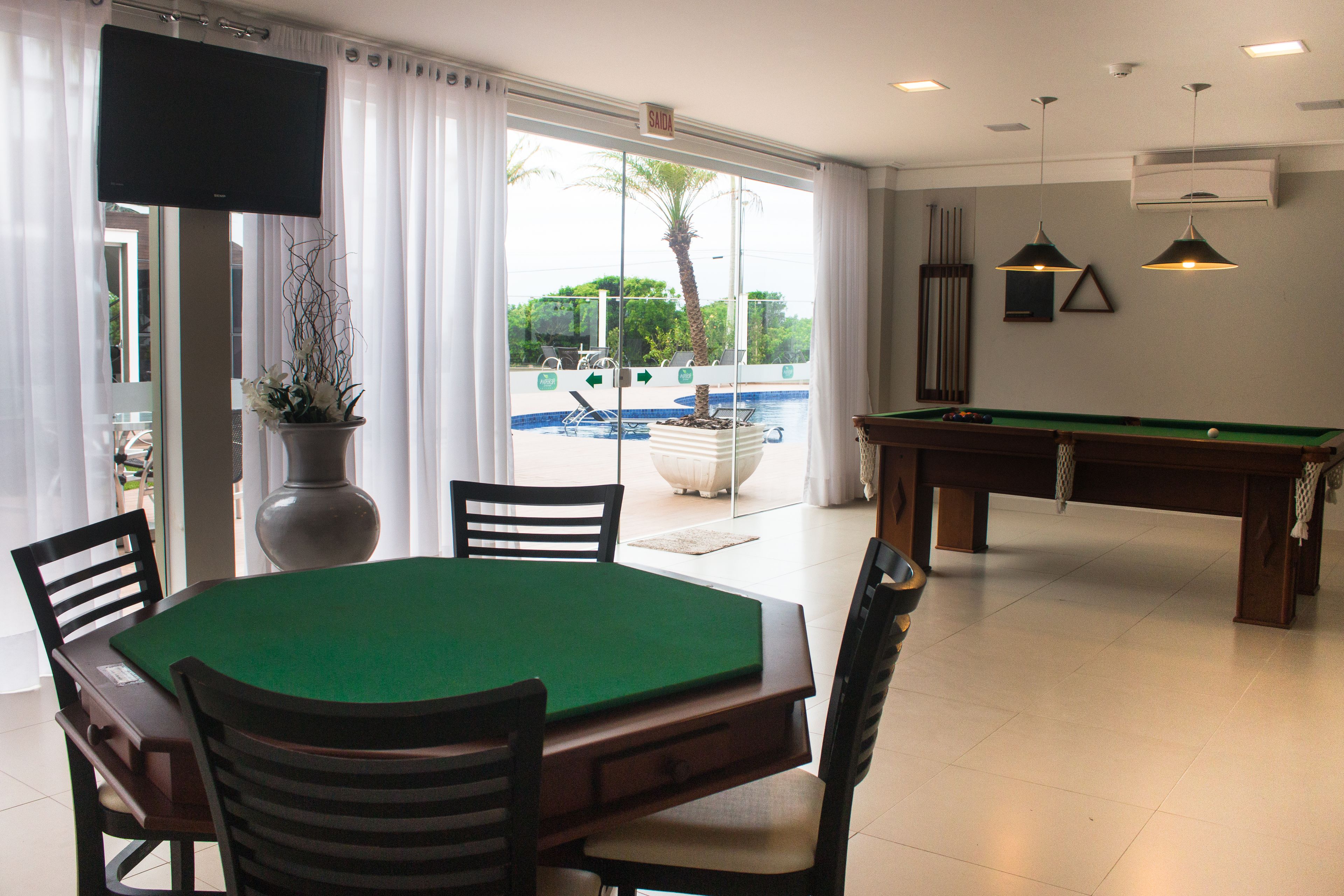 Ein Billardtisch mit Stühlen, einem Fernseher und Blick auf den Pool.