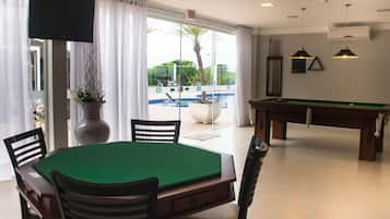 Ein Billardtisch mit Stühlen, einem Fernseher und Blick auf den Pool.