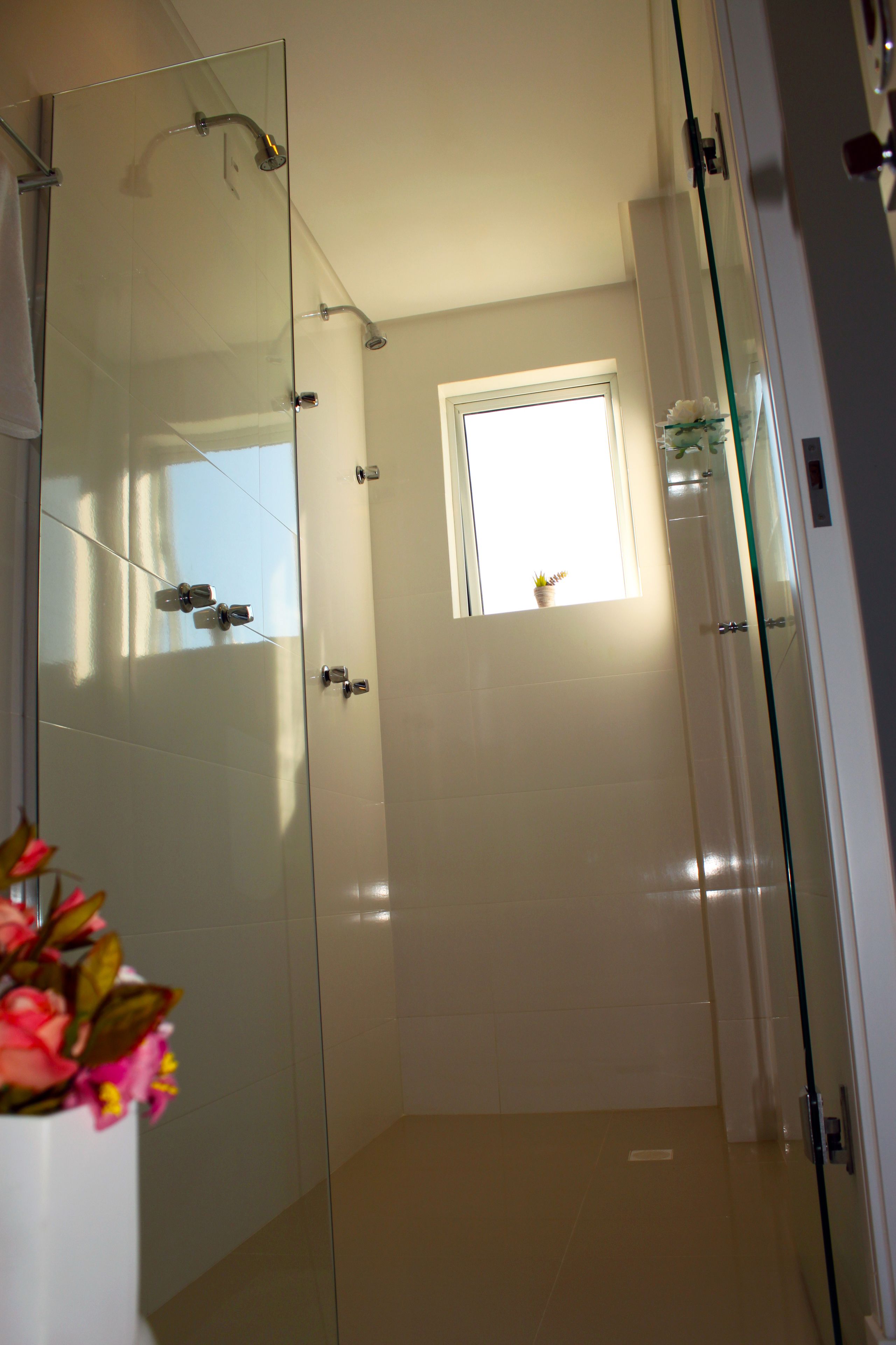 Un baño moderno con cabina de ducha de vidrio, un ventanal pequeño y una planta en maceta.