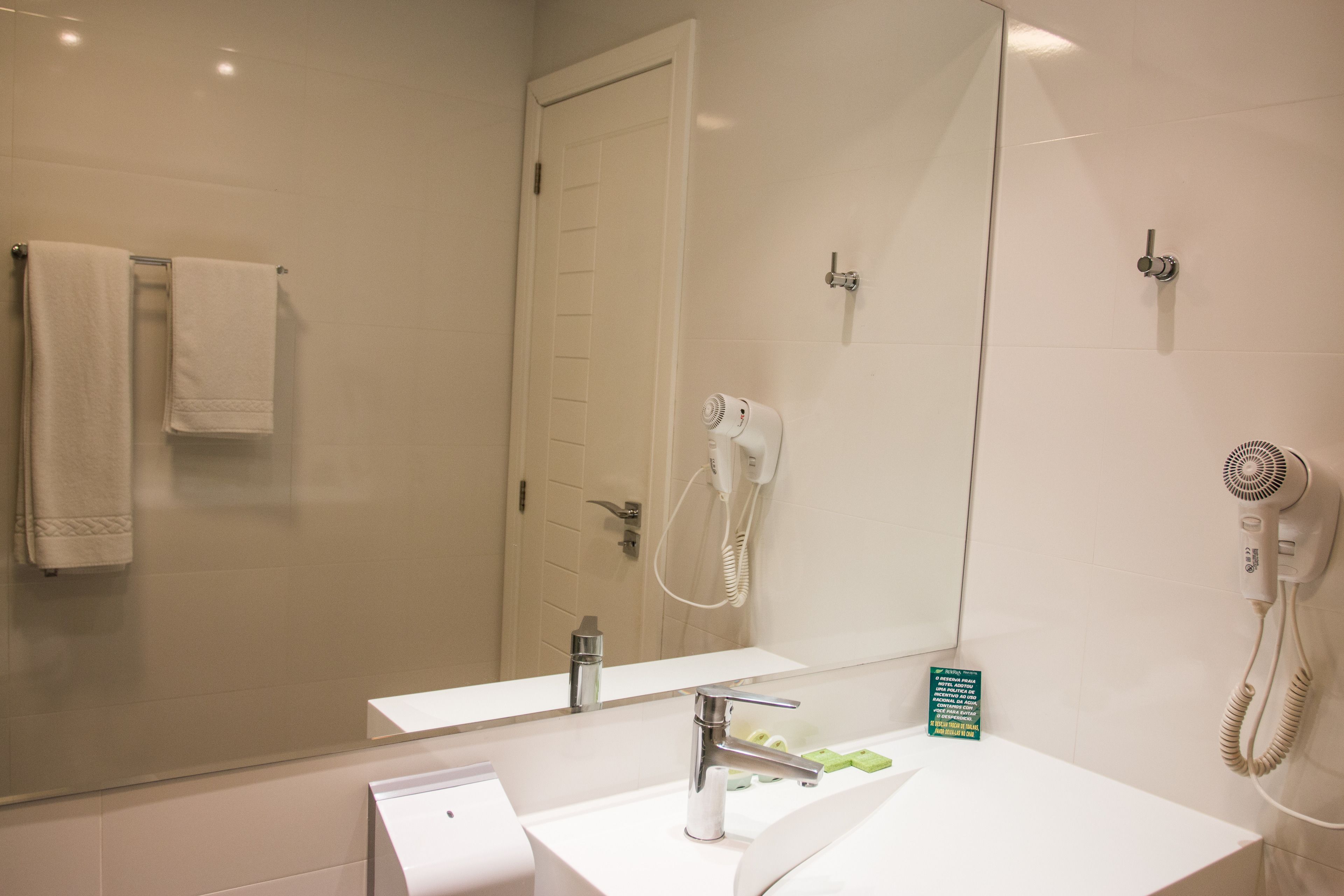 A modern bathroom with a white sink, a mirror, a towel rack, and a hairdryer.