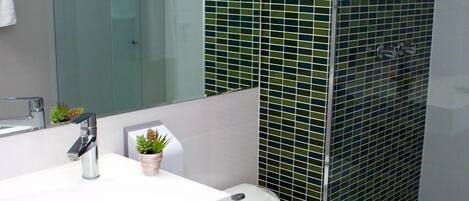 Egy modern fürőszoba, fehér mosdókagylóval, WC-vel és üveg válaszfallal ellátott zuhanyzóval.