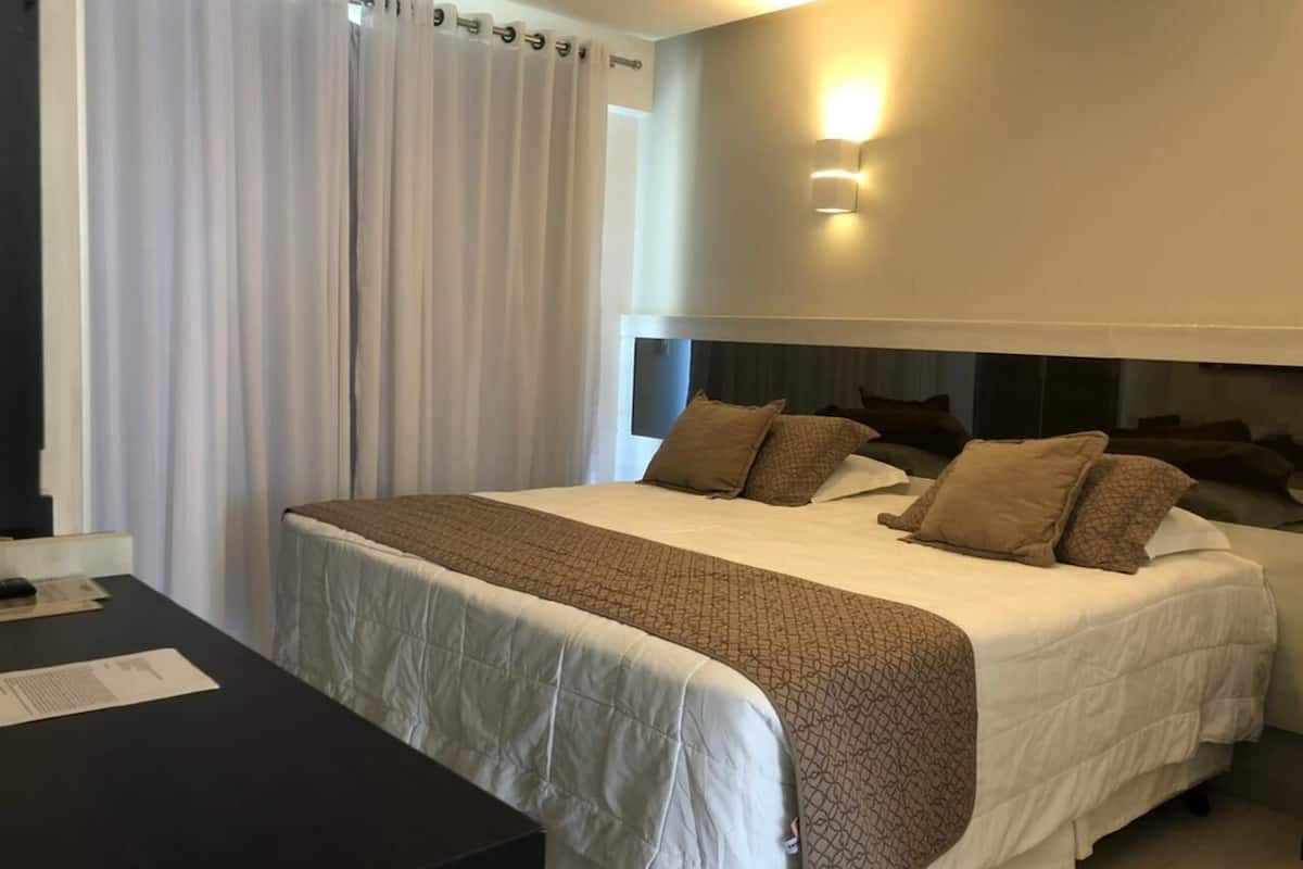 A hotel room with a large bed, a desk, and a curtain.