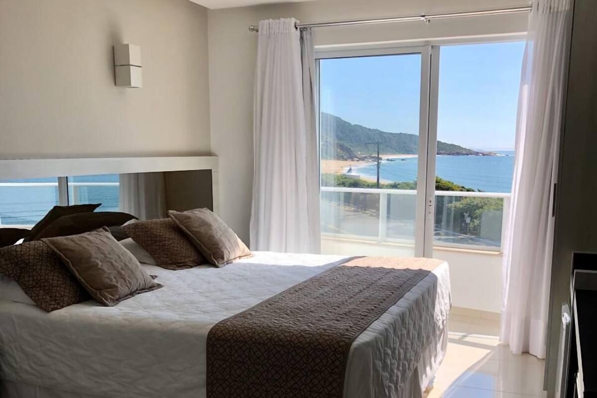 A hotel room with a large bed, a view of the sea, and a balcony.