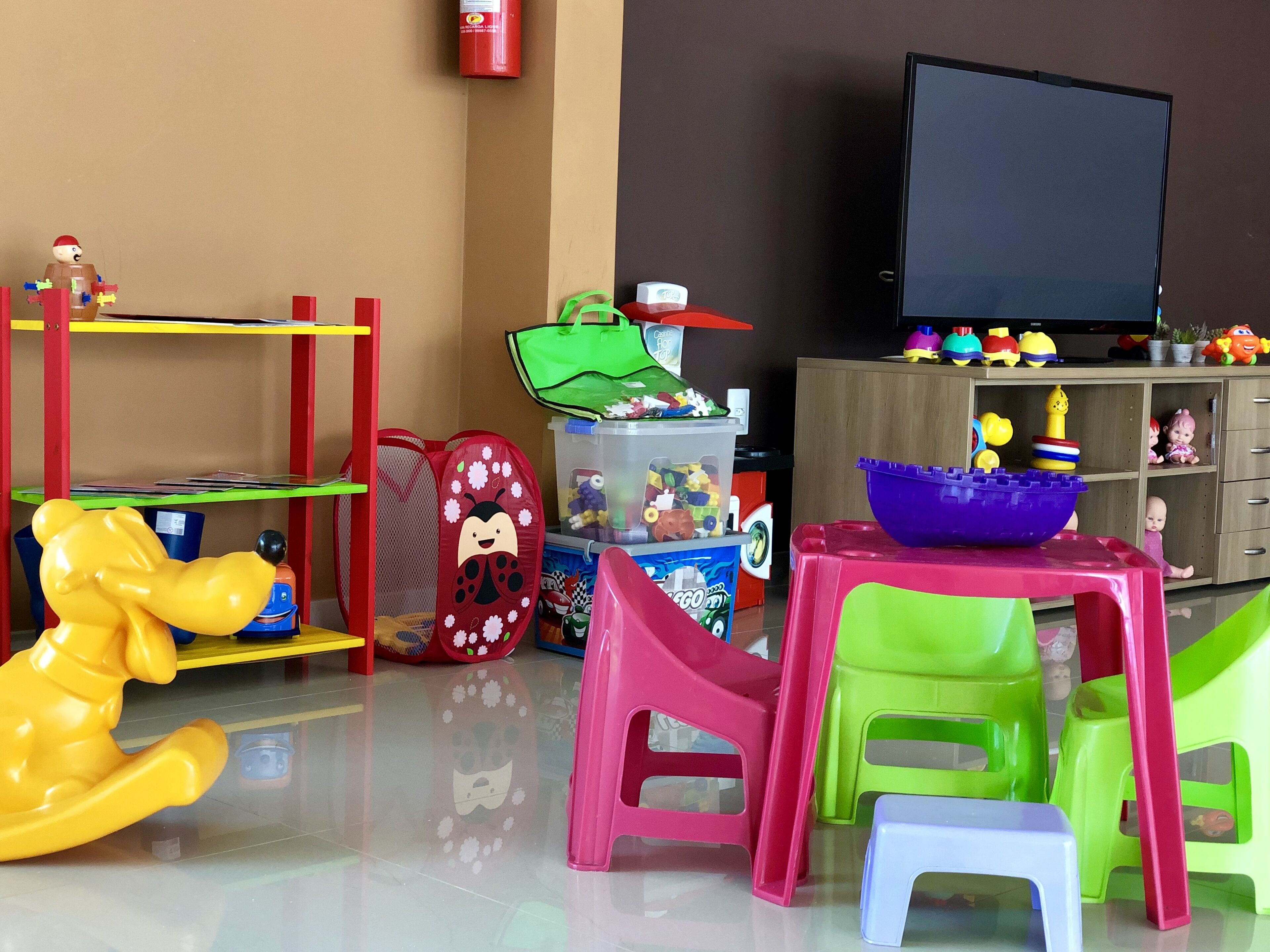 Un espace de jeux avec des jouets en plastique de couleurs vives, une télévision et un meuble de rangement.