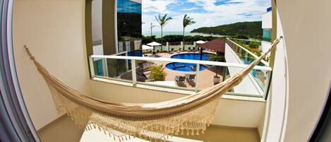 A hammock on a balcony overlooking a pool and a beach.