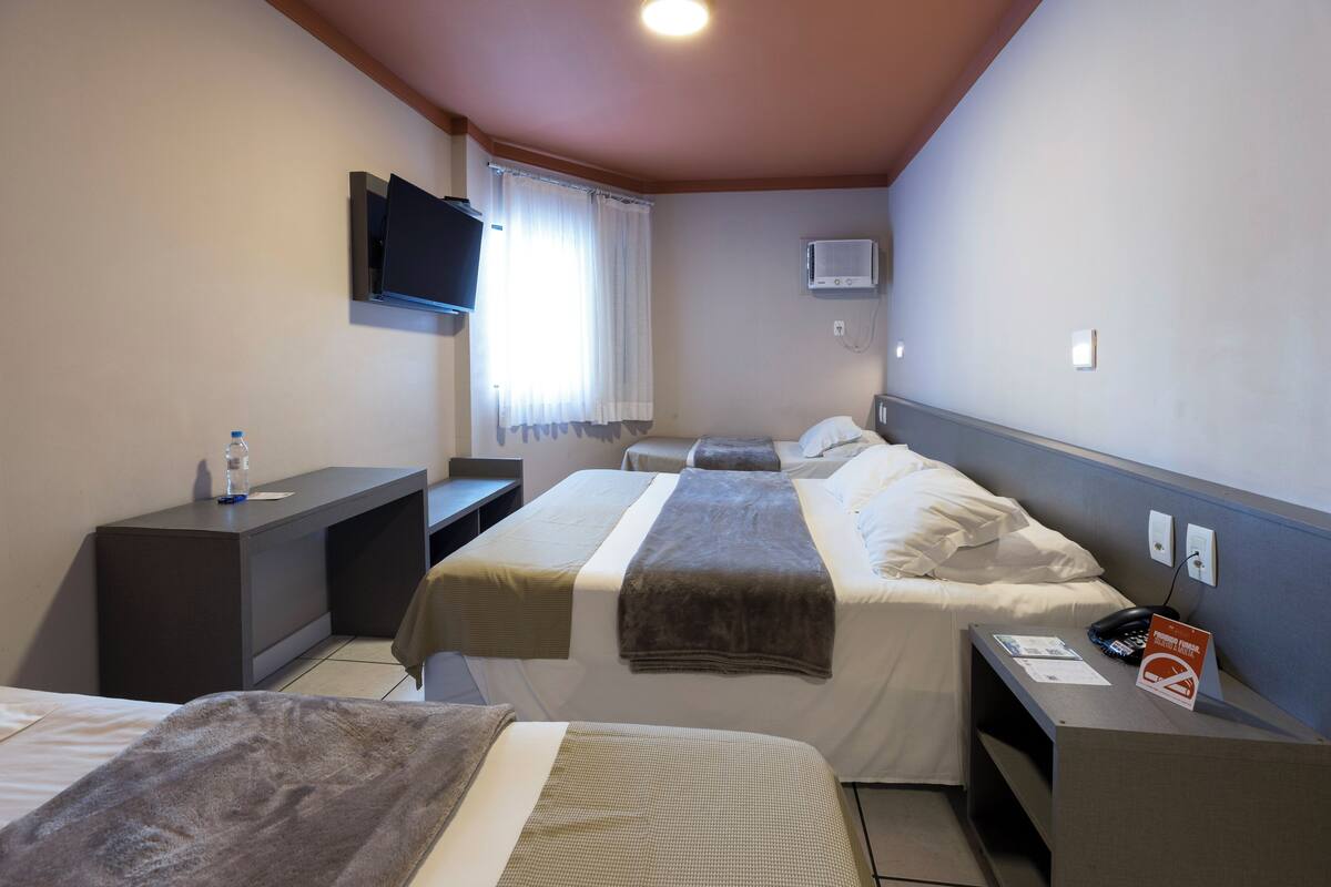 A hotel room with two beds, a desk, a TV, and a minibar.