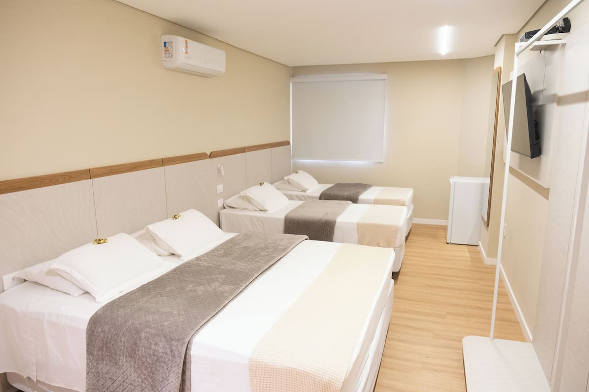 A hotel room with two single beds, a TV mounted on the wall, and a window with a blind.