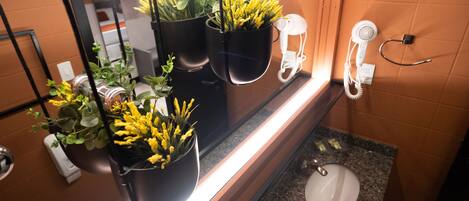 Un baño con lavamanos, espejo y tres macetas colgantes con flores amarillas.