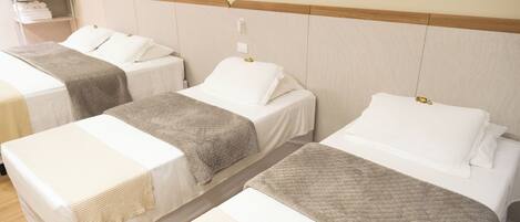 Habitación de hotel con tres camas individuales, cada una con cabecero de madera y ropa de cama blanca.