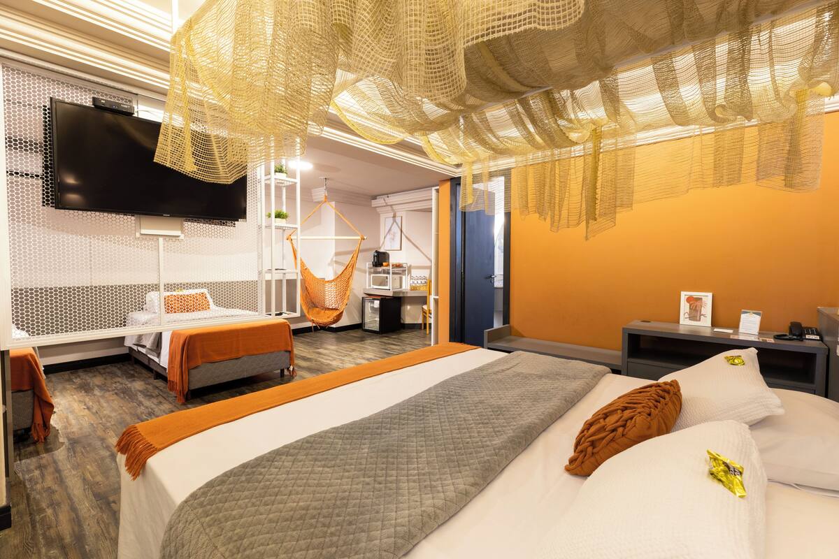 A hotel room with a bed, a TV, a hanging chair, and a desk with a chair.