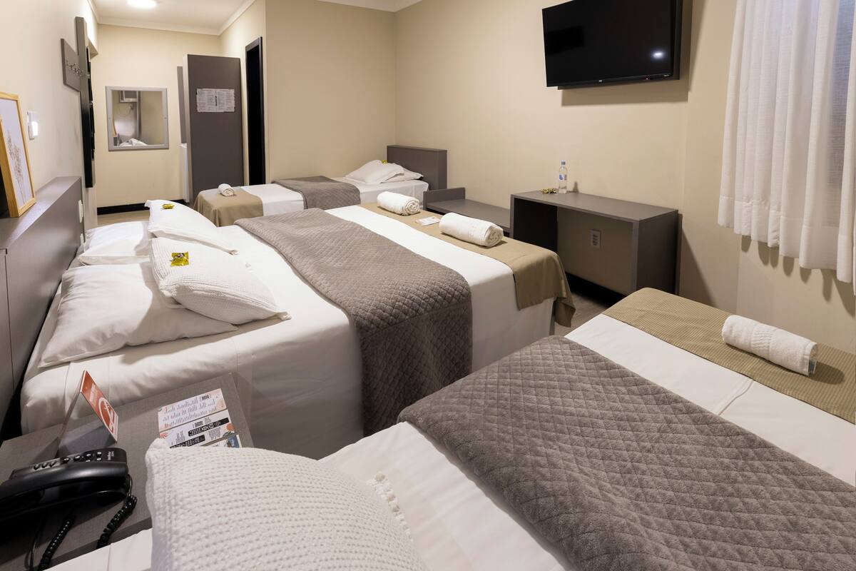 Ein Hotelzimmer mit drei Betten, einem Fernseher, einem Schreibtisch und einem Telefon.