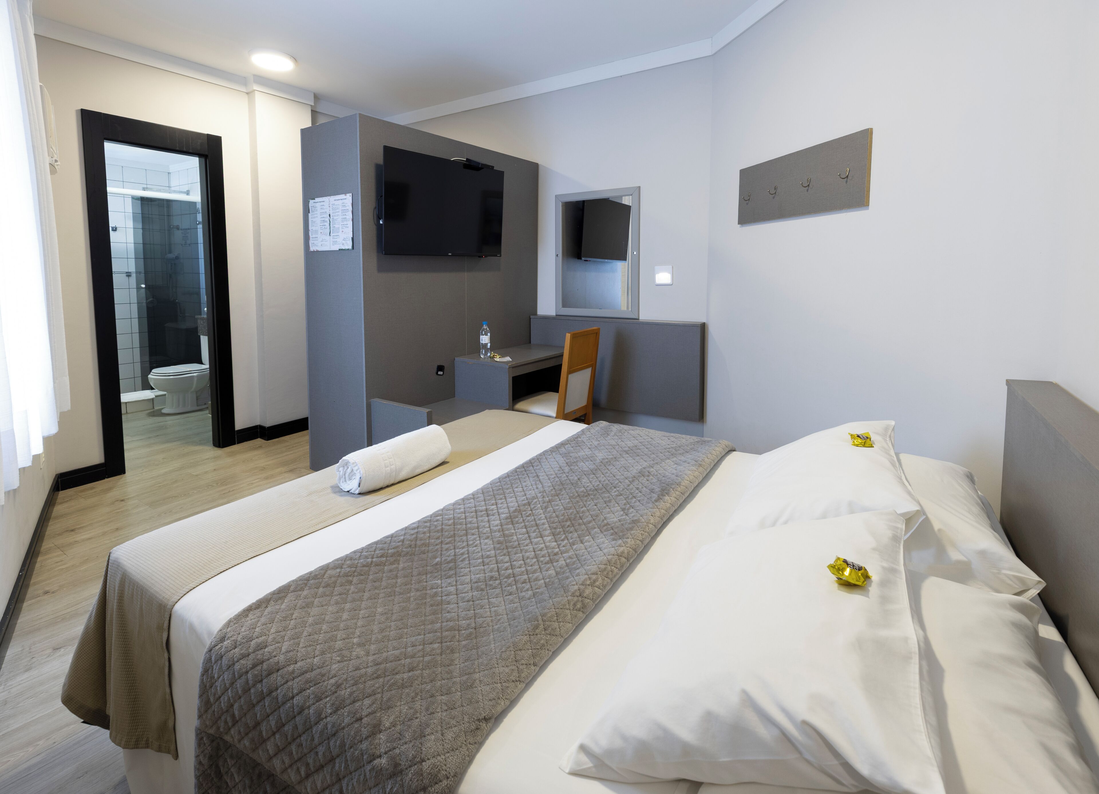 A hotel room with a bed, a desk, a chair, a television, and a bathroom visible through an open door.