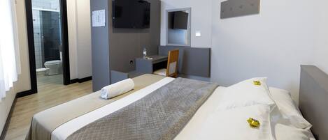 A hotel room with a bed, a desk, a chair, a television, and a bathroom visible through an open door.