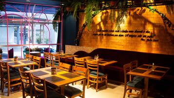 A restaurant interior with wooden tables and chairs, a brick wall with a quote, and potted plants.