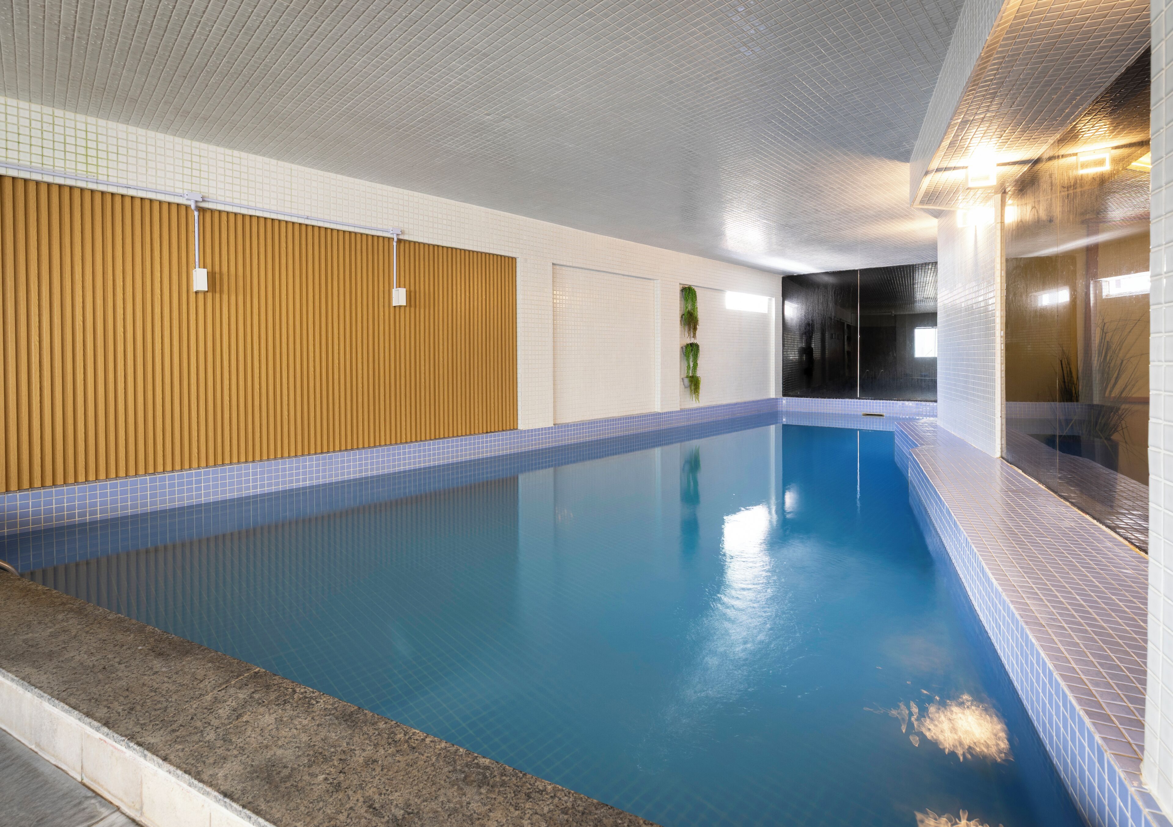 Ein Innenpool mit gefliesten Wänden, einer Holzpaneelwand und einem gefliesten Boden.
