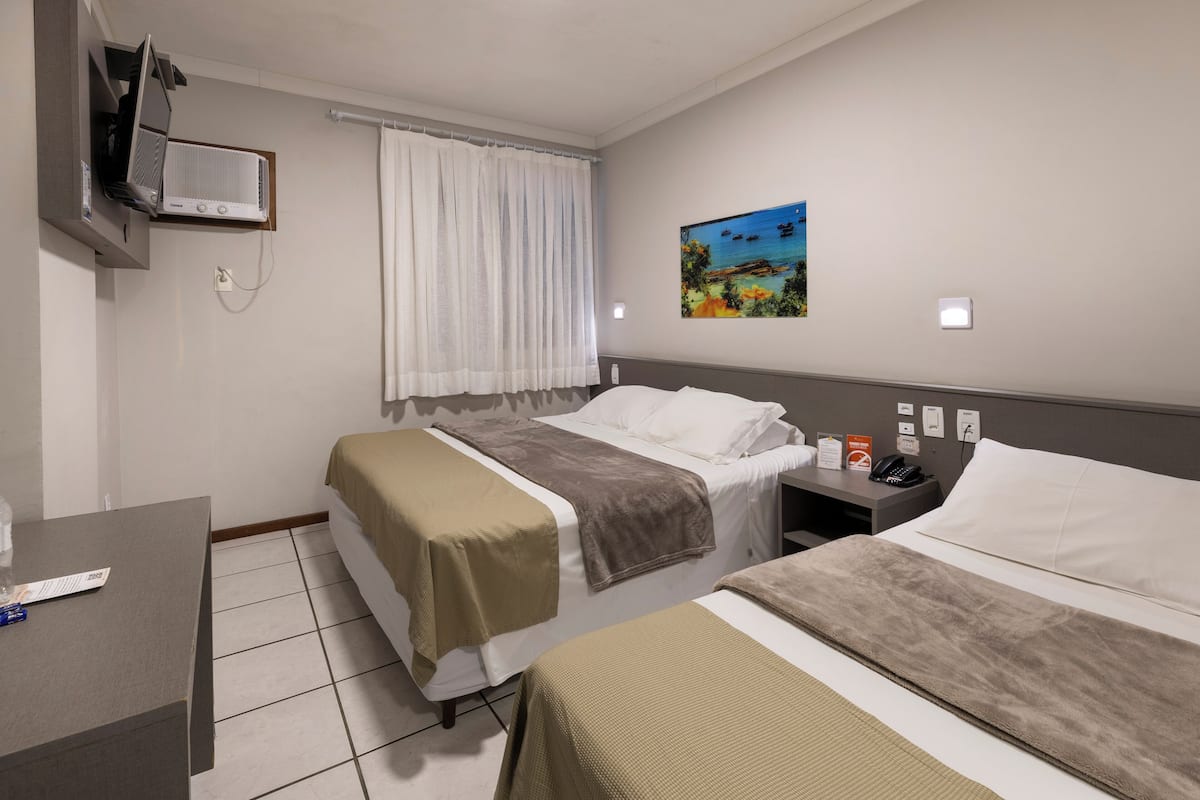 A hotel room with two beds, a desk, a TV, and a painting on the wall.