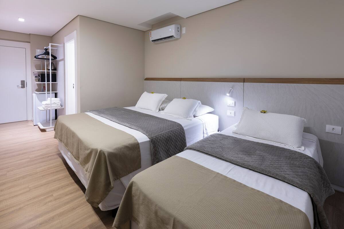 A hotel room with two beds, a wardrobe, a shelf unit, and an air conditioning unit.