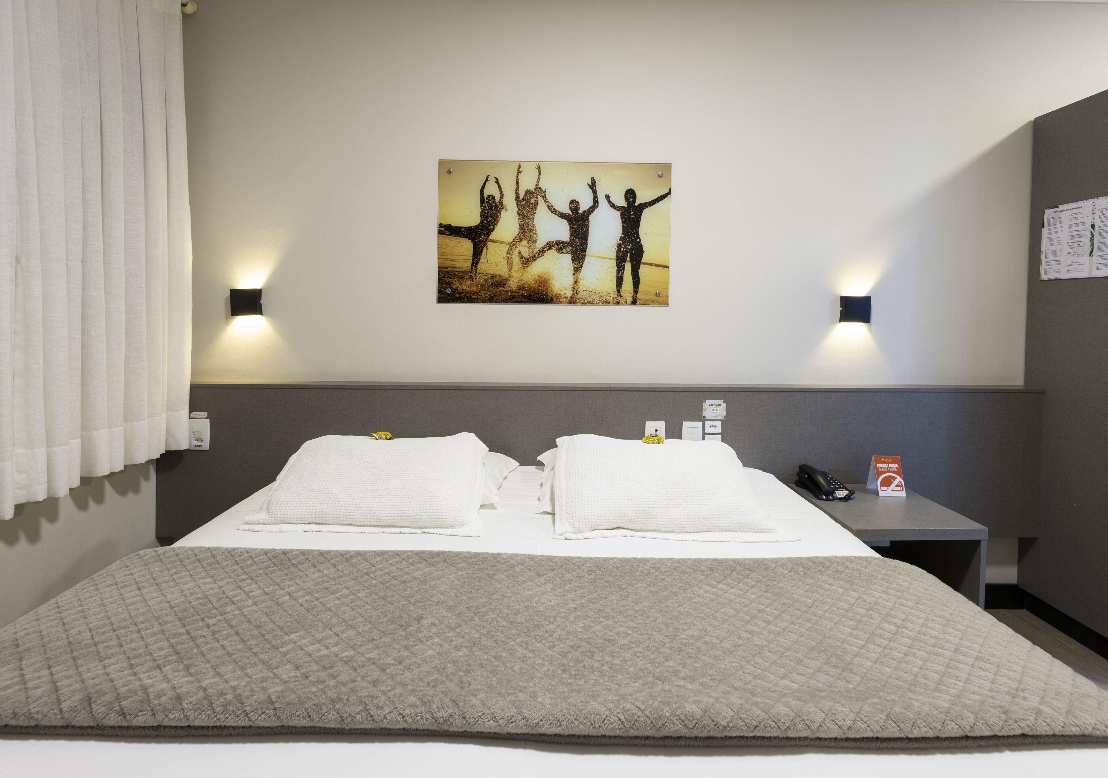 A hotel room with a bed, two wall-mounted lights, a painting, a nightstand, and a telephone.