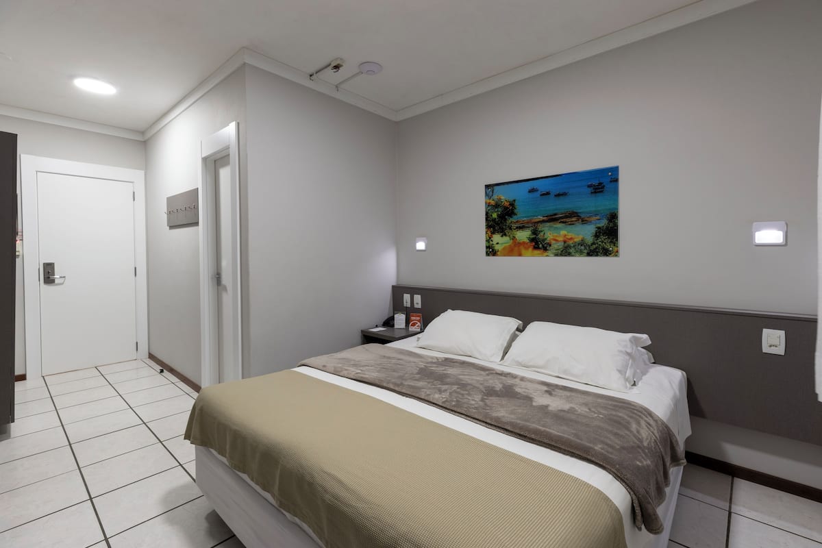 A bedroom with a bed, a nightstand, a painting on the wall, and a door.