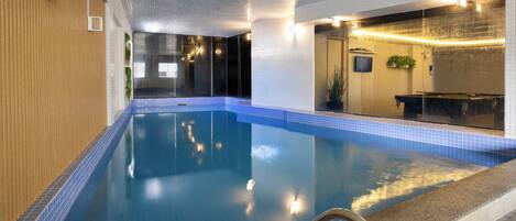 Una piscina interior con agua cristalina, una pared de madera en un lado y una pared de azulejos en el otro.