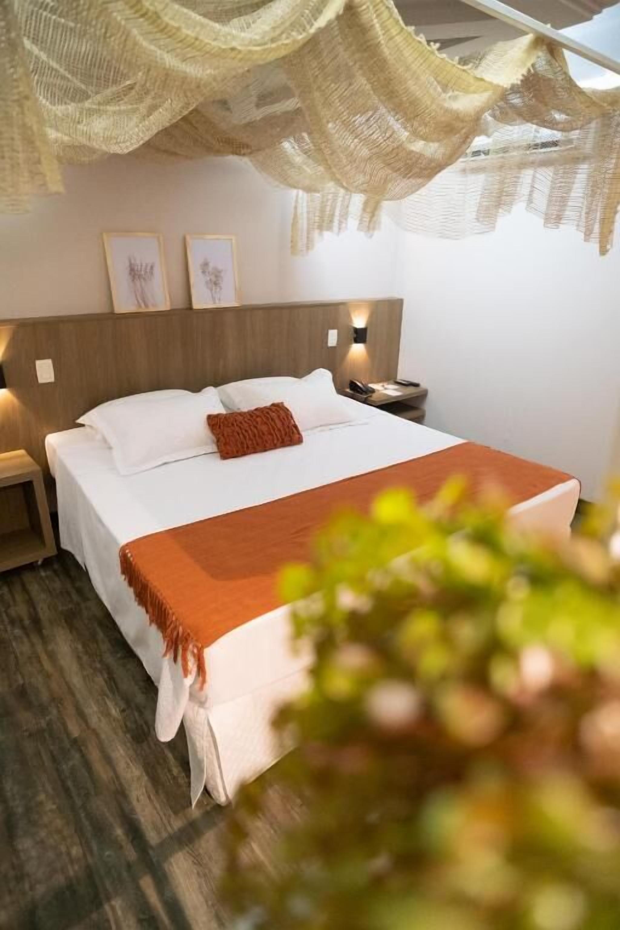 Un letto rifatto con lenzuola bianche e una coperta marrone, una lampada da comodino e un quadro appeso al muro.