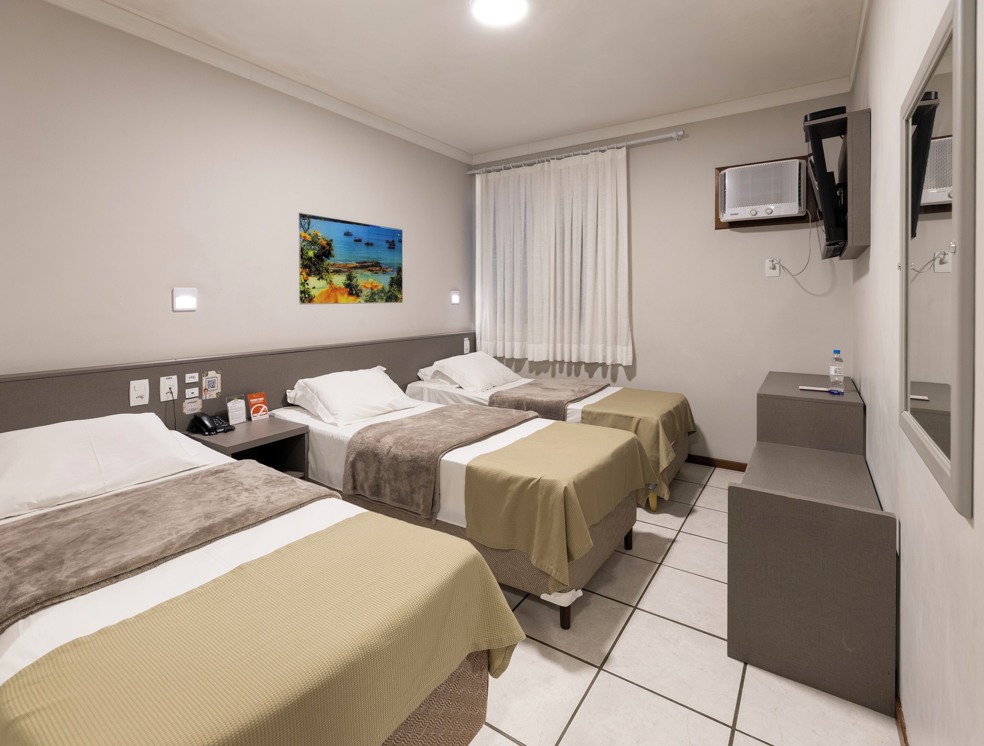 Habitación de hotel con tres camas, un escritorio, una silla, un cuadro, una ventana con cortinas y un televisor.