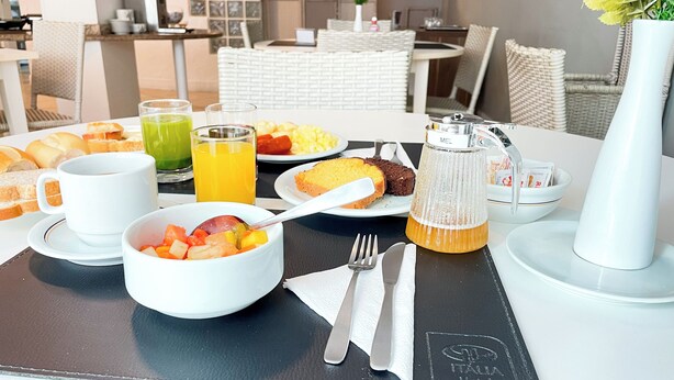 A breakfast setting with a variety of food items, including toast, fruit, and a muffin, along with beverages and a coffee maker. - Hotel Itália (Balneário Camboriú)
