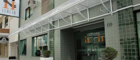 A modern hotel entrance with a glass door, a signboard, and a covered walkway.