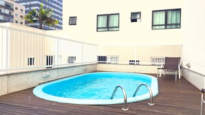 A rooftop swimming pool with a wooden deck, a chair, and a palm tree. - Hotel Itália (Balneário Camboriú)