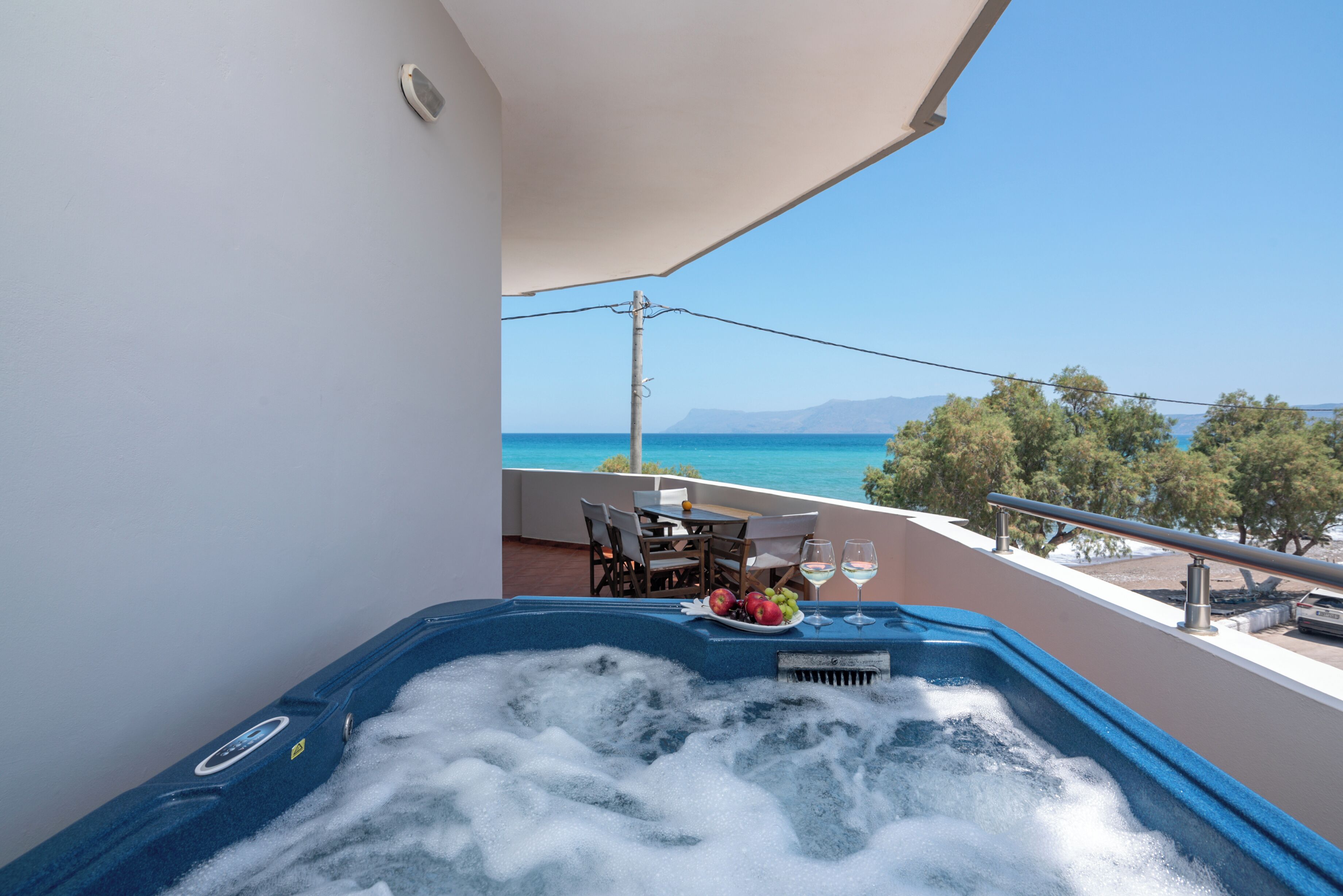 A balcony with a hot tub, a table with chairs, and a view of the sea.