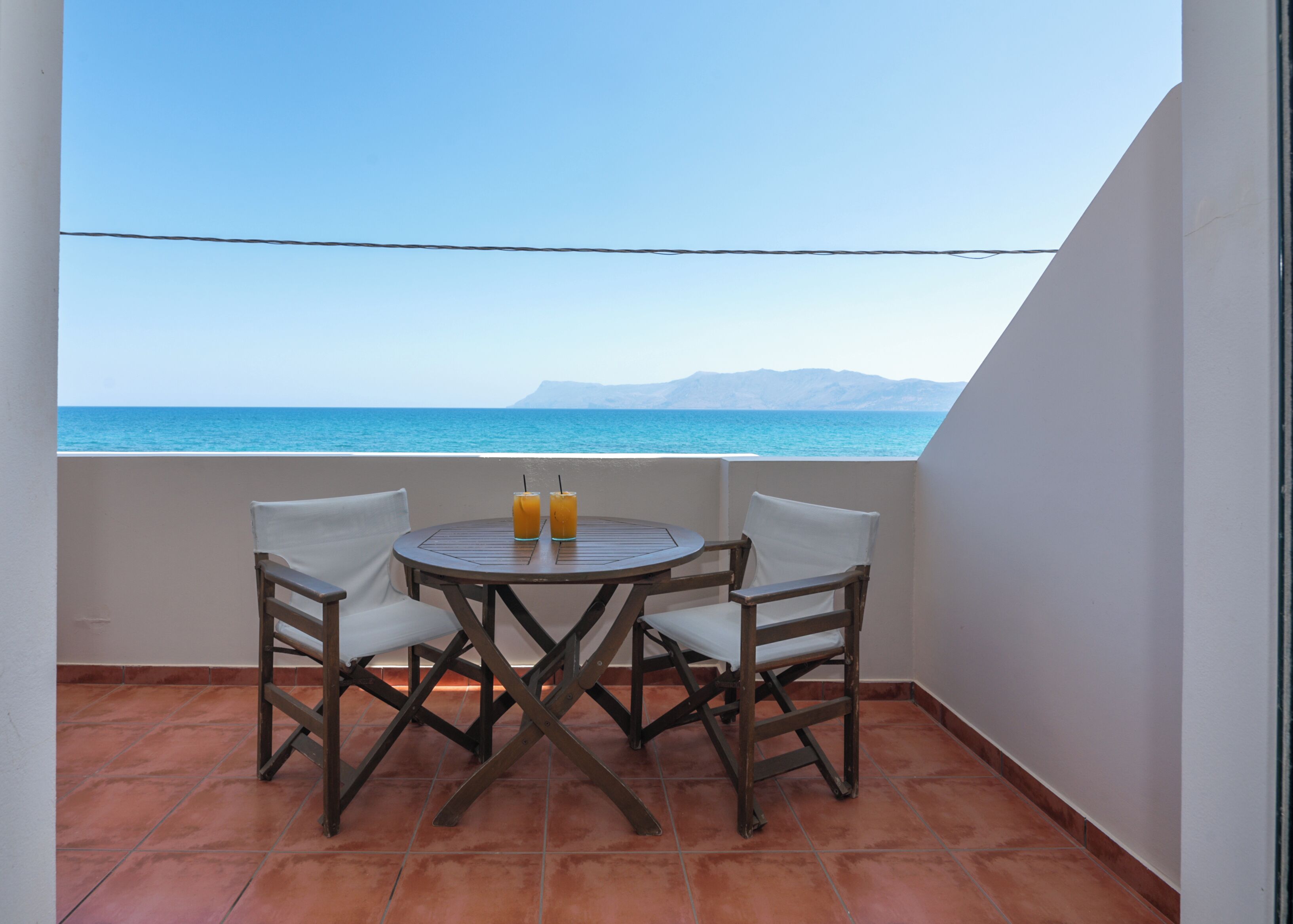 Un balcón con una mesa y dos sillas, con vista a una masa de agua y montañas distantes.