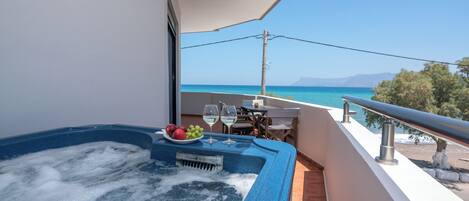 A balcony with a hot tub, table, and chairs, overlooking a clear blue sea and distant mountains.