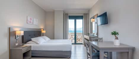 A hotel room with a bed, bedside tables, a desk, a chair, a TV, and a balcony with a view.