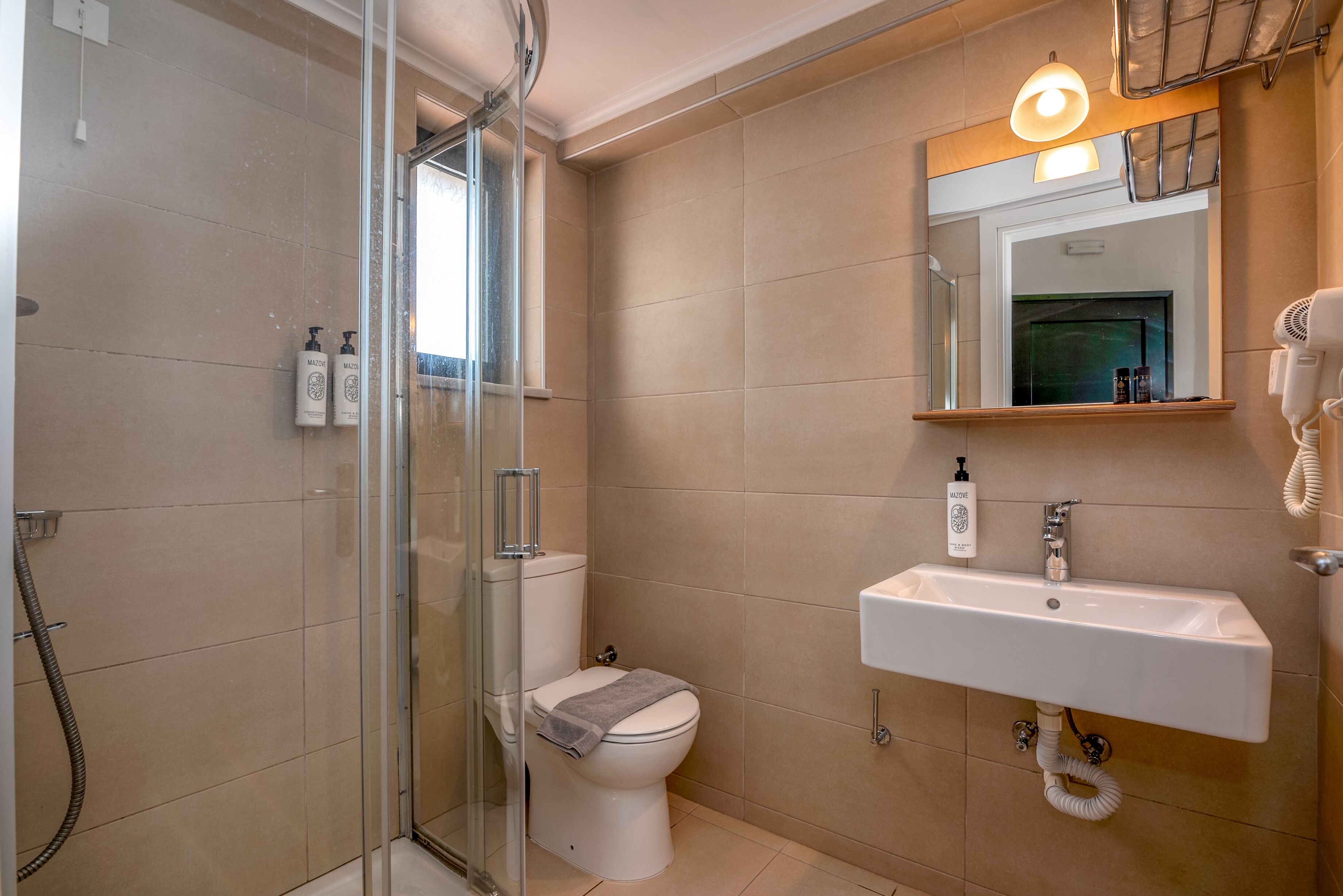 A bathroom with a glass shower enclosure, a toilet, a sink with a mirror, and a hairdryer on the wall.
