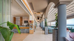 En hotellobby med en receptionsdisk, en sittgrupp och stora fönster med utsikt över havet.