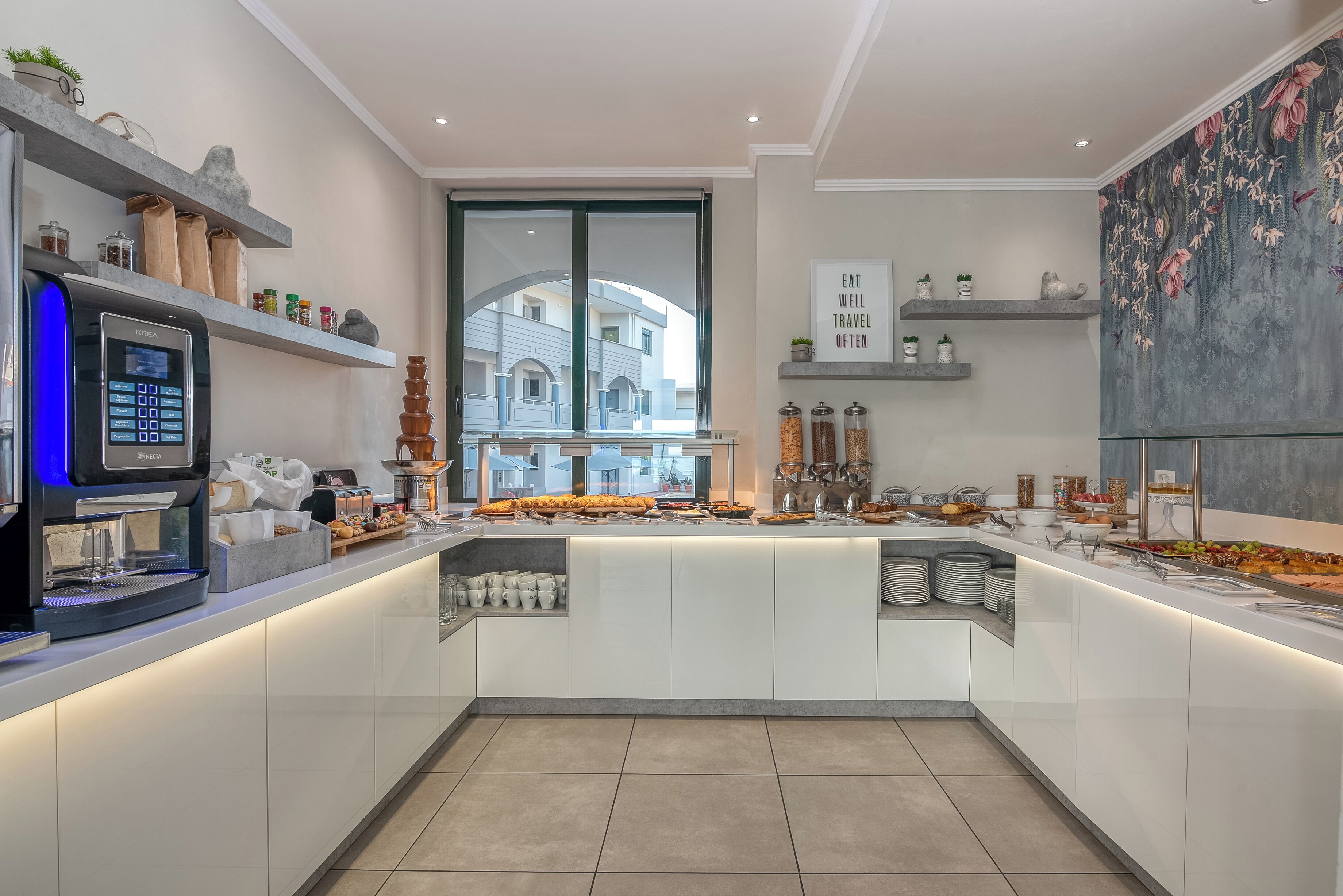 Una cocina moderna con cafetera integrada, un ventanal grande y vista a un edificio.