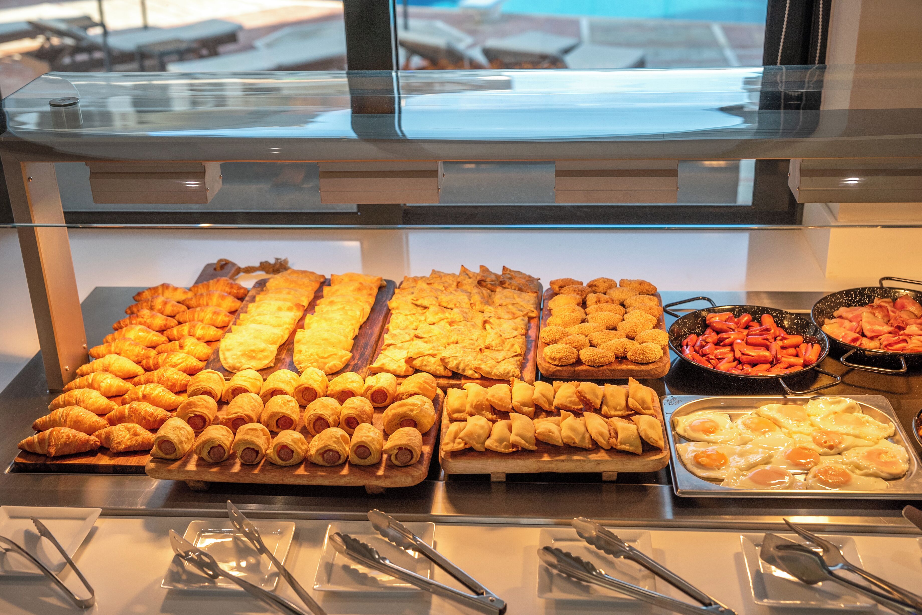 A buffet with various food items including pastries, hot dogs, and eggs.