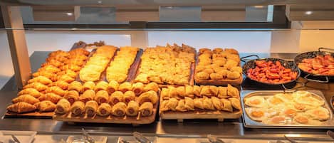 A buffet with various food items including pastries, hot dogs, and eggs.