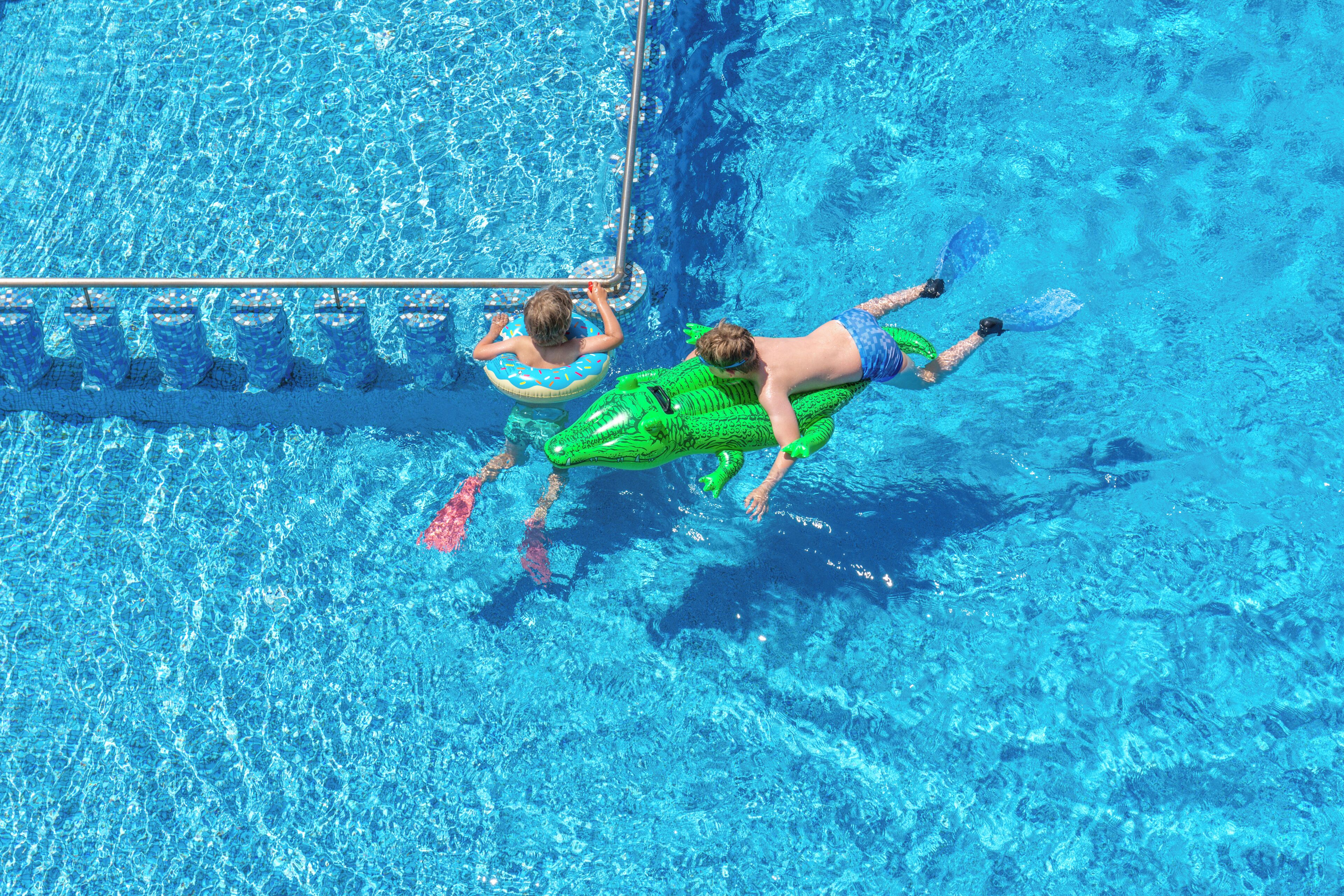 A swimming pool with clear blue water, a diving board, and inflatable floats.