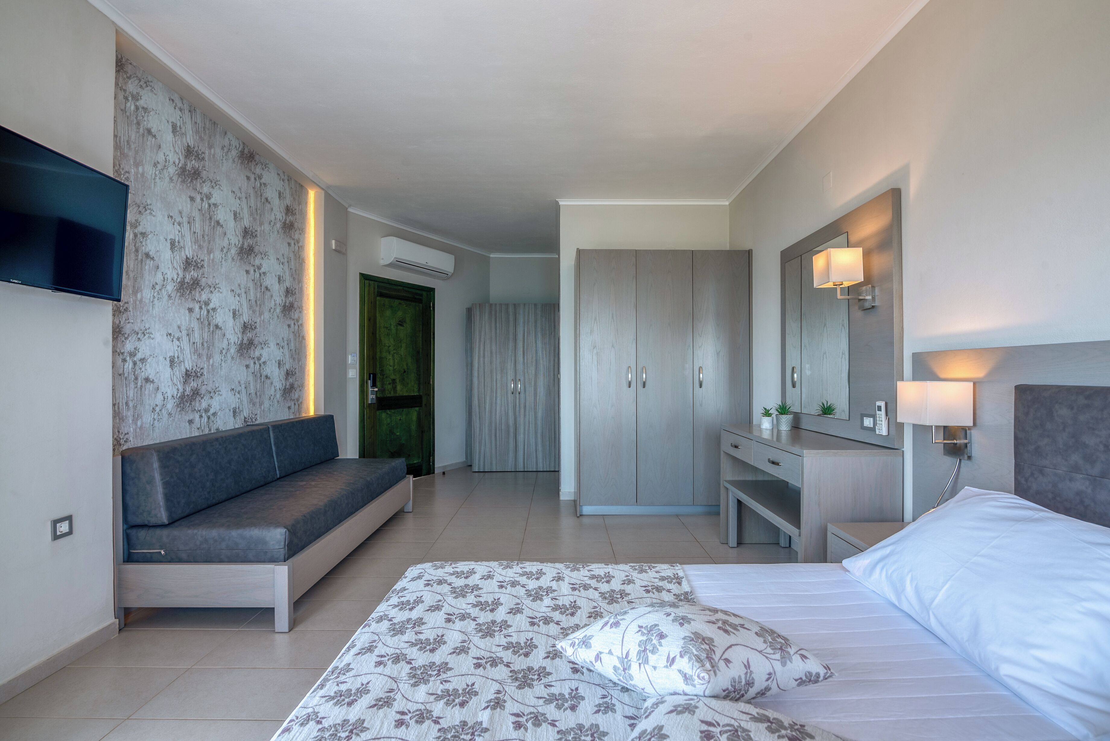 A modern hotel room with a bed, sofa, desk, and wardrobe.
